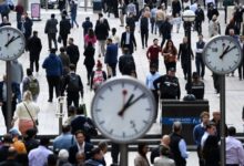 A busy scene at Canary Wharf in London, showing a large crowd of workers walking through the area.