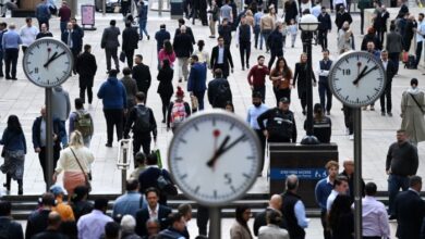 A busy scene at Canary Wharf in London, showing a large crowd of workers walking through the area.