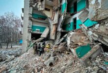 Rescue workers are clearing rubble from a severely damaged residential building. The structure is partially collapsed, with debris scattered around