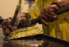 A mine worker wearing protective gloves hammers a large gold ingot after removing it from its mold