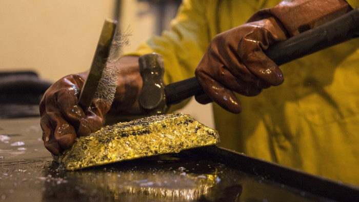 A mine worker wearing protective gloves hammers a large gold ingot after removing it from its mold