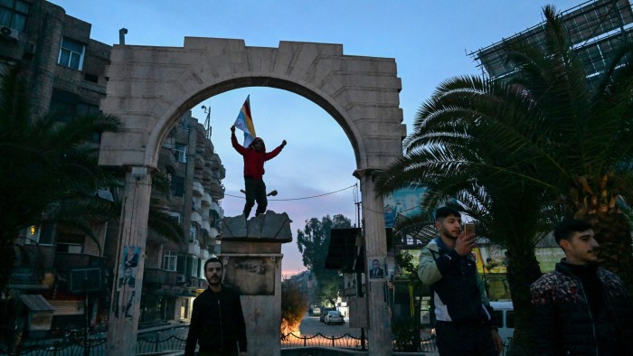 Cheering men walk past an arch on a Damascus street at daybreak on December 8